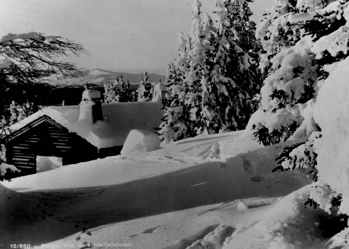 Avfotografert postkort. Laftet tømmerhytte i snødekt granskog ved Gålå høyfjellshotell. I forgrunnen sees skispor i snøen.