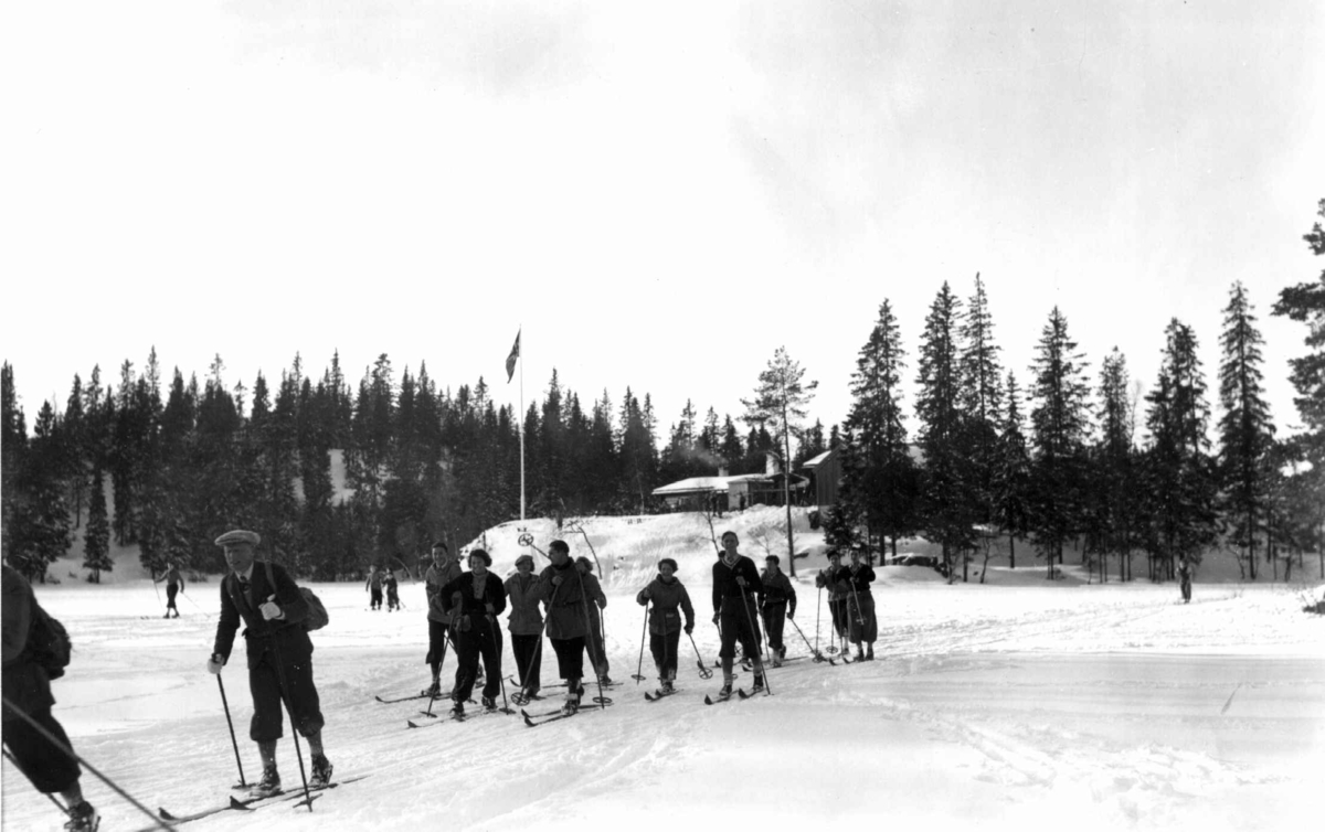 Skiløpere i Nordmarka, Oslo. 1934. Tryvannstua med flagget til topps ses i bakgrunnen. 
