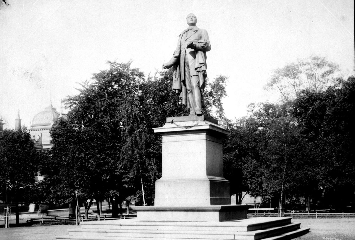 Statue av Henrik Wergeland (1808-45) på Eidsvolds Plass, Oslo. Statuen er i bronse, laget av Brynjulf Bergslien i 1881. T.v. ses tårnet på Christiania Tivoli (bygget 1890, revet 1934). Del av Brødrene Brunskows serie norske landskapsbilder.