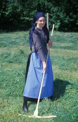 Kvinne iført drakt, i arbeid på jordet, hvor hun raker samme