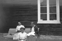 Tre kvinner sitter utenfor et hus på en benk og driver med h