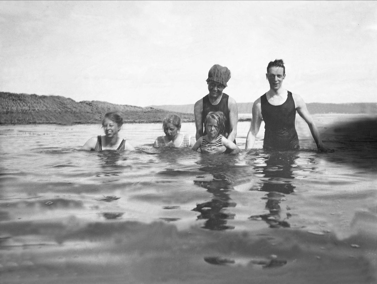 Voksne og barn kledd med badedrakt bader i sjøen. Robsahm og Lund.