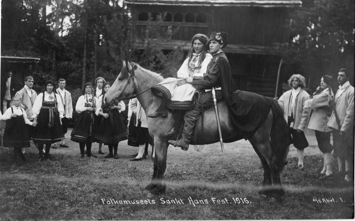 Postkort. Kvinne og mann på hest. Norsk Folkemuseums St. Hansfest 1916.