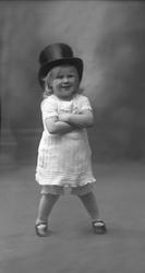 Portrett, lite barn med flosshatt og armene i kors.