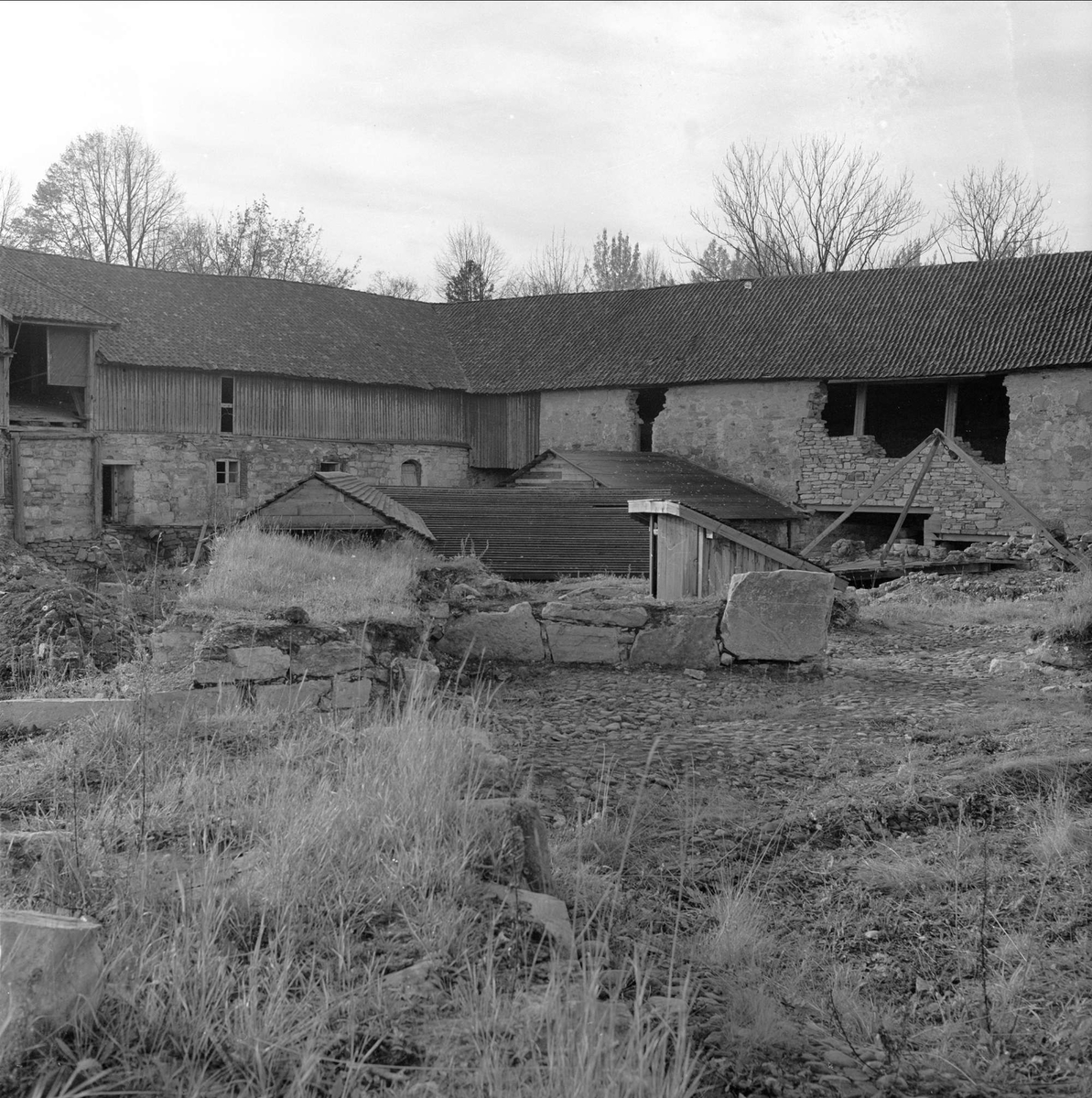 Domkirkeodden, Hamar, 22.10.1957. De fremgravde ruinene fra bispegårdsutgravingen. Murkronene er dekket med midlertidig tak. Bak ligger Storhamarlåven.