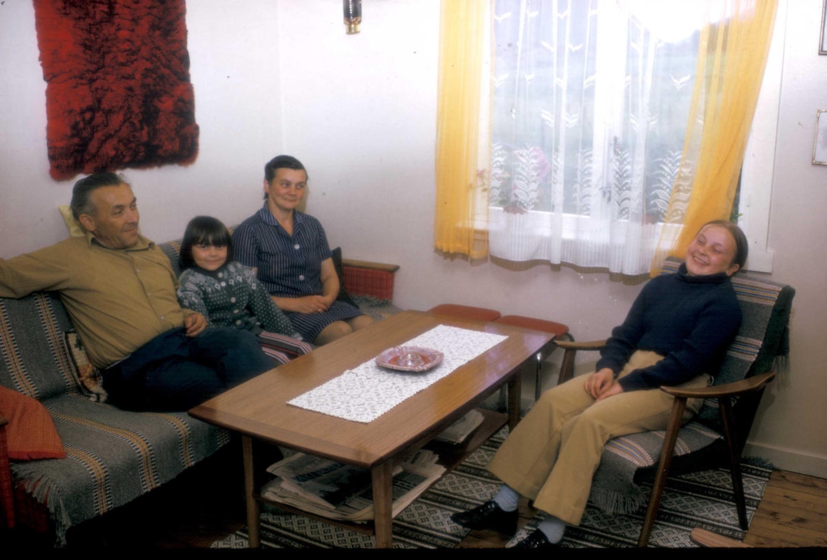 Familie i stua, Oliva Blomsterli og Nils Hansen med to barn, 1973, Manndalen, Kåfjord, Troms. Mary sitter mellom foreldrene, Nora i stolen til høyre.