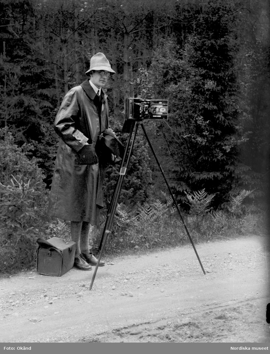Gösta Berg, amanuens och senare styresman vid Nordiska museet, står vid en kamera monterad på stativ under en byundersökning i Dalarna