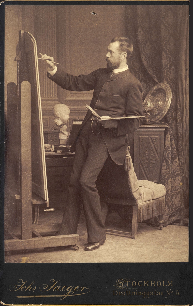Konstnären Julius Kronberg (1850-1921) målar vid sitt staffli. Kabinettsporträtt.
