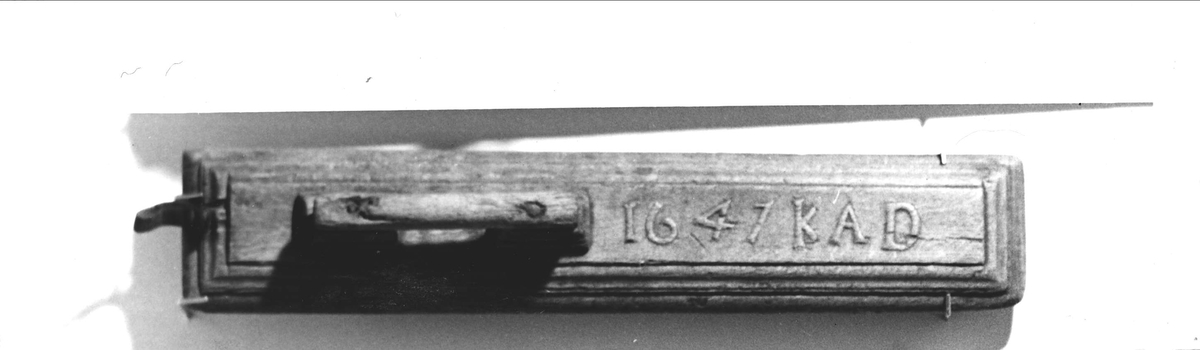 Mangelbräde av ek. I relief skuret: 1647 K A D. Spikat handtag. På ena kortsidan påspikad upphängningsögla av läder. Tillhörande mangelrulle av trä.