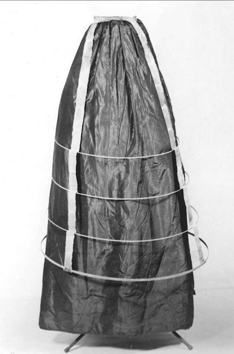 Krinolin av bruna trådklädda metallringar, som hålls på plats med bruna mönstrade band. Linning av vita och bruna kyprade band med spänne.

