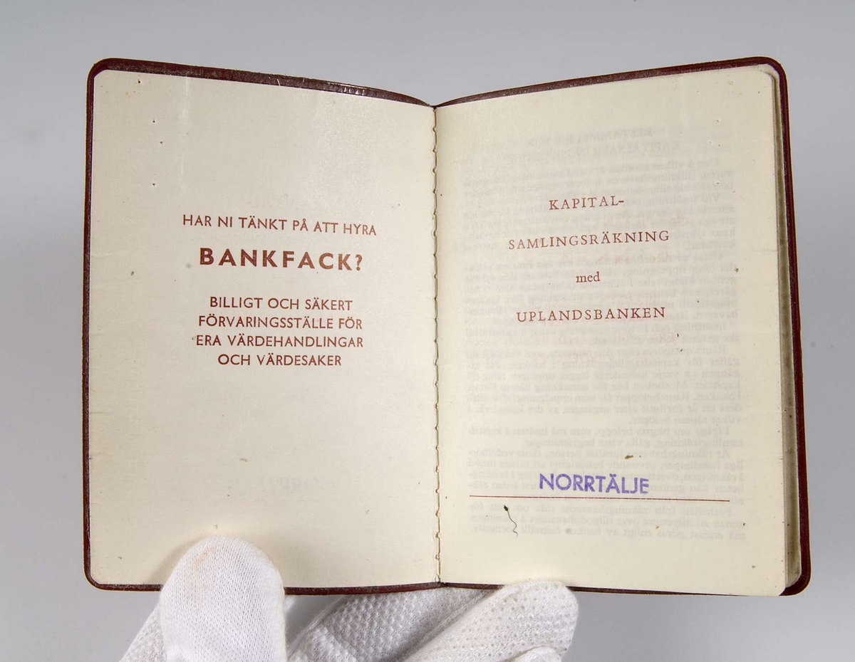 Vinröd bankbok av plast, en läderimitation. Uplandsbankens logotype på framsidan.

