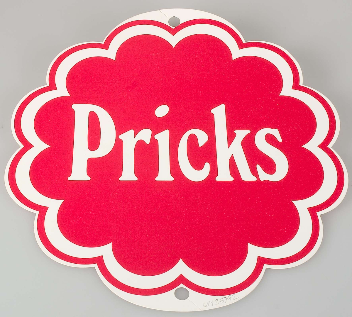 En skylt av papp, formad som en pepparkaka, med hål både upptill och nedtill, tryck i rött: Pricks logotype.
