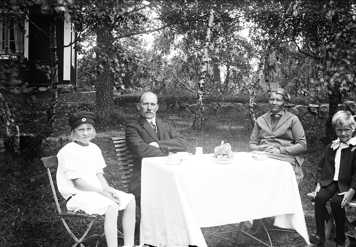 Kvinna, man och barn vid kaffebord i trädgården, sannolikt Uppland, eventuellt 1925