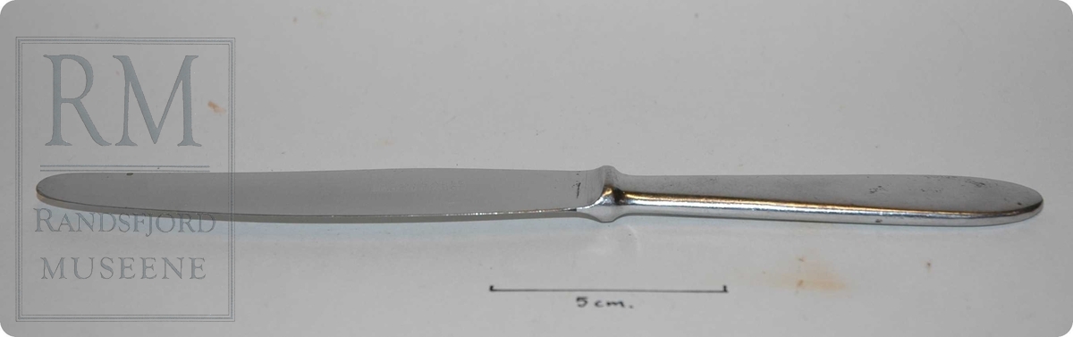 Stål, av et stykke, skaft tilnærmet rektangulært tverrsnitt med avrundede kanter. Forhøyning mellom skaft og knivblad.