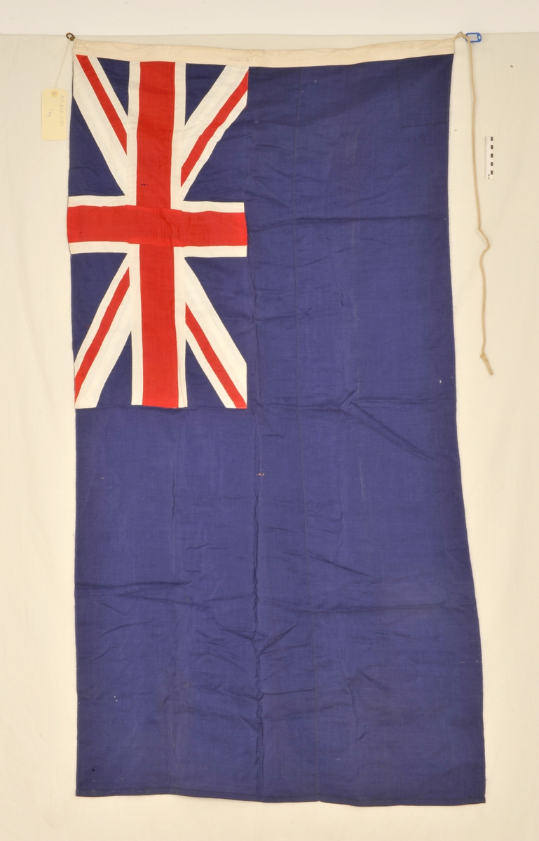 Flagg av grovt tekstil. En fjerdedel av flagget er dekket av det britiske flagget, resten er blått.Næmest stangen er det innsydd en taustump, som i flaggets øvre del ender i en metallring.