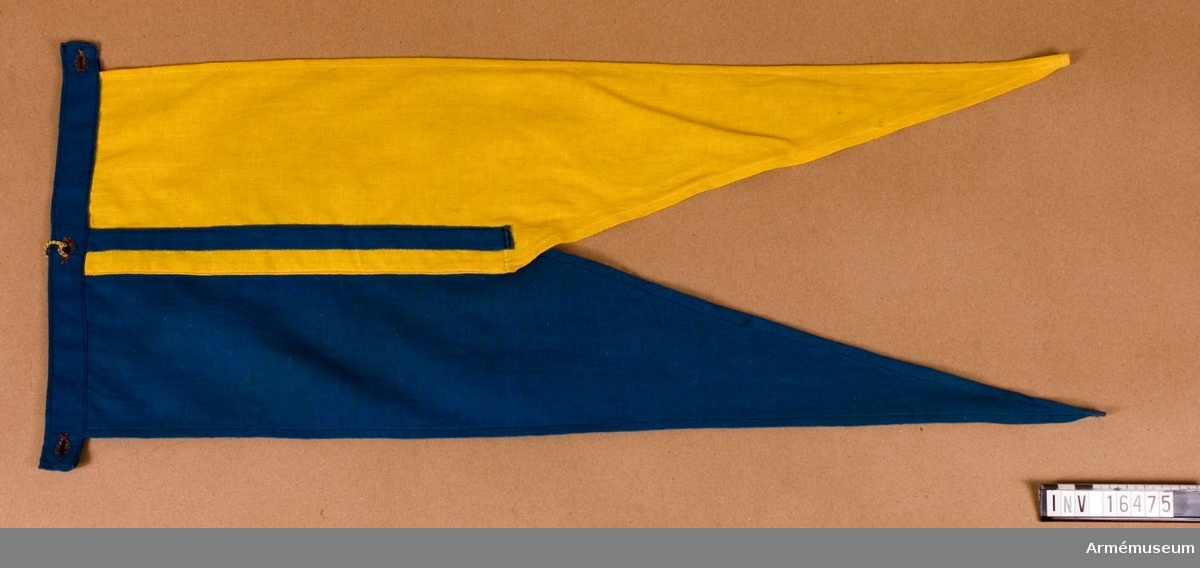 Tillverkad av blå och gul bomullsduk, så kallad flaggduk. Fästes på lans m/1851 med det blå partiet uppåt, överst.