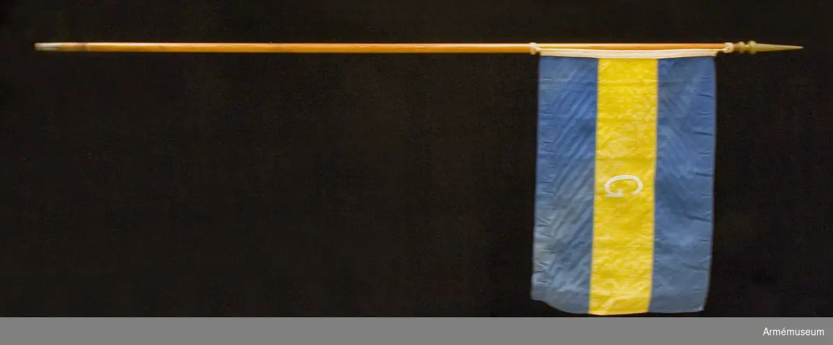 Enkel flagga i linne på trästång med svarvad knopp målad i guld. Utförd av Stockholms flaggfabrik AB.