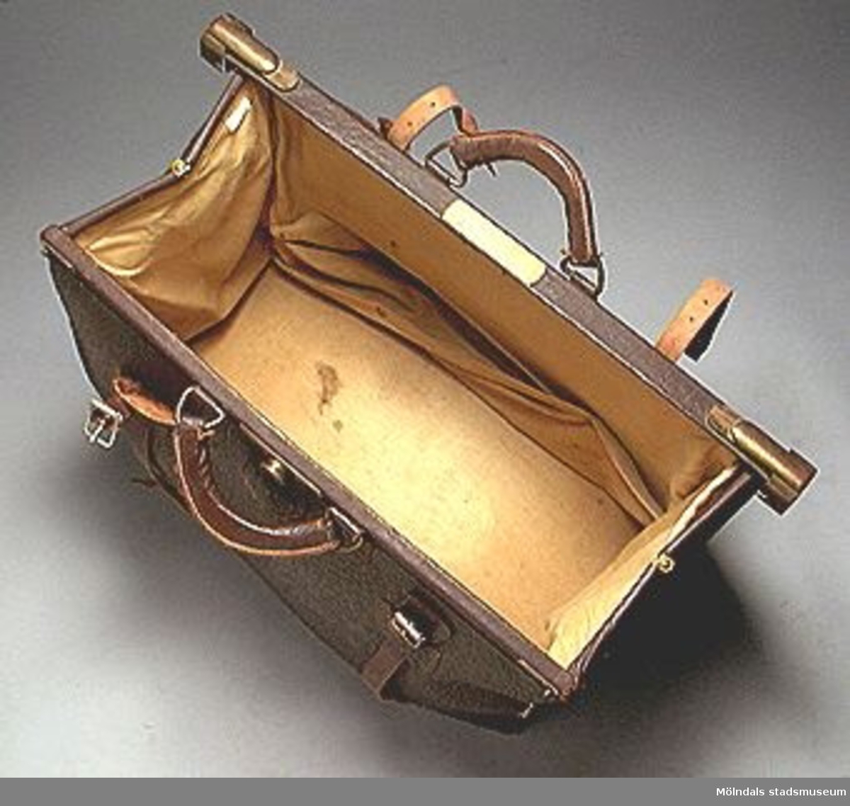 Brun läderkoffert med två handtag. Mässingslås och två remmar runt med spännen. Ägaren var ärkebiskop Erling Eidems amma. Hon skänkte kofferten till givarens mor på 1930-talet. 