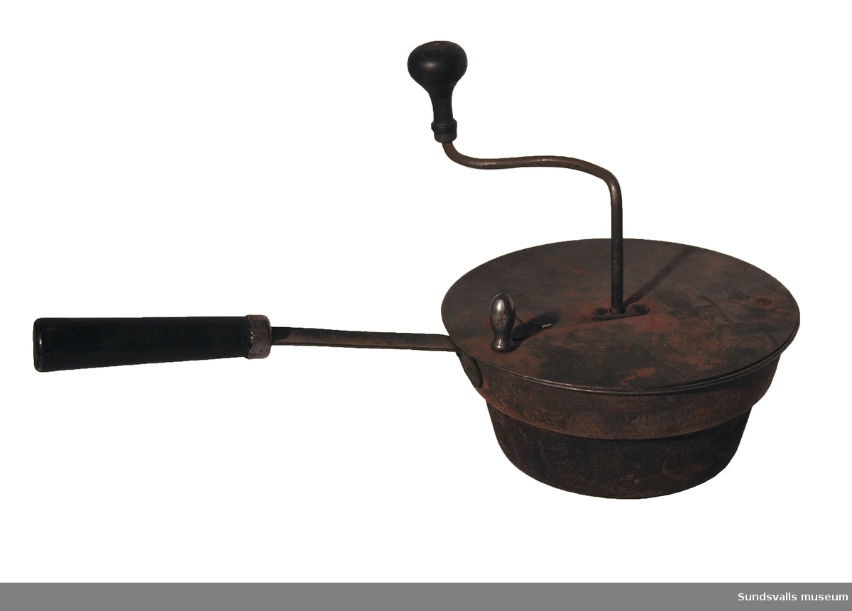 Kaffebrännare i form av en kastrull med handtag av metall och trä, samt en vev med träknopp genom locket. Avsedd för rostning av kaffe på en järnspis. Genom att snurra veven rörs kaffebönorna om inne i brännaren. Halva locket kan öppnas genom att det förs åt sidan.