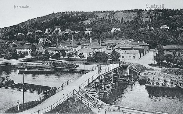 Vy över Norrmalm. Gamla gångbron (kallad Puckelbron och Kamelryggen) över Selångersån. Bron låg i Norrlandsgatans förlängning. Bron raserades 1919 vid den stora vårfloden. Den ersattes med en ny bro, som också kallades Puckelbron, i Malmskillnadsgatans förlängning. Vykort.