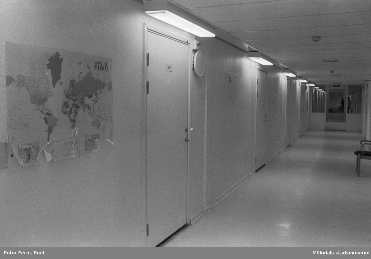 Dokumentation av Sagåsens flyktingförläggning 1992. En lång korridor med stängda dörrar. En världskarta hänger på vänsterväggen och lite längre ner i korridoren står en stol utefter en vägg.