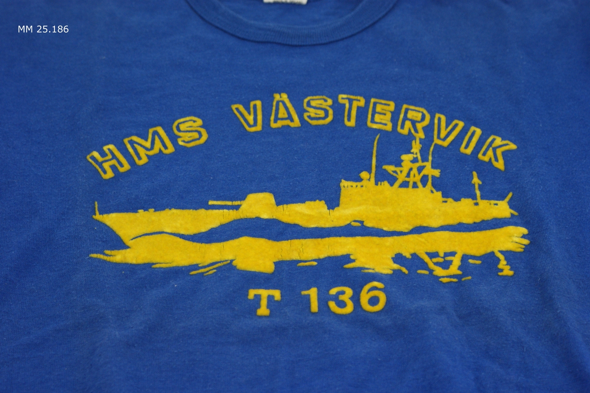 Marinblå kortärmad t-shirt med gult tryck i plyschaktigt material. Text: "HMS Västervik T 136" och en torpedbåt till sjöss.