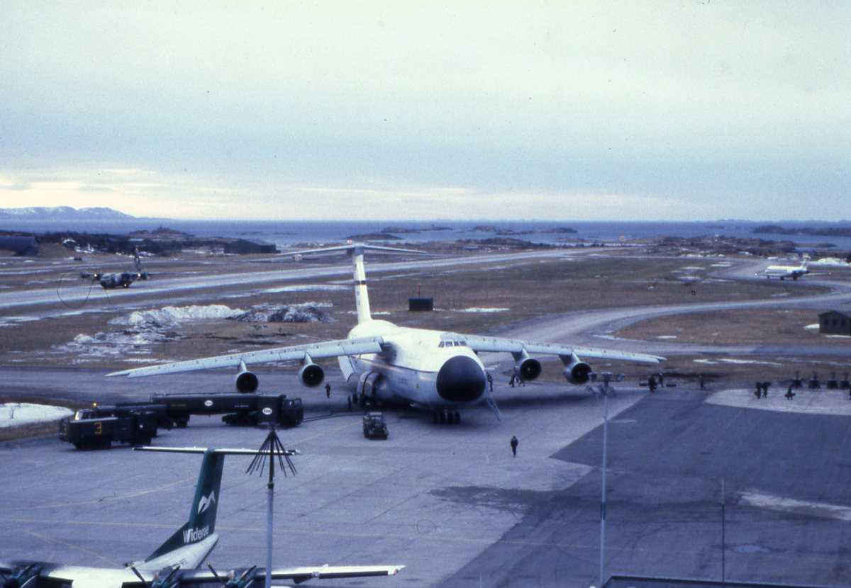 Amerikansk fly av typen Lockheed  C-5 Galaxy sees midt i bildet. Widerøe sitt Dash 7 fly sees til venstre og nede i bildekanten. SAS sitt fly sees til høyre og på midten i bildet. Forsvarets C-130 Hercules sees på rullebanen til venstre om midt i bildet, og flyet tilhører 335 skvadron på Gardermoen flystasjon.