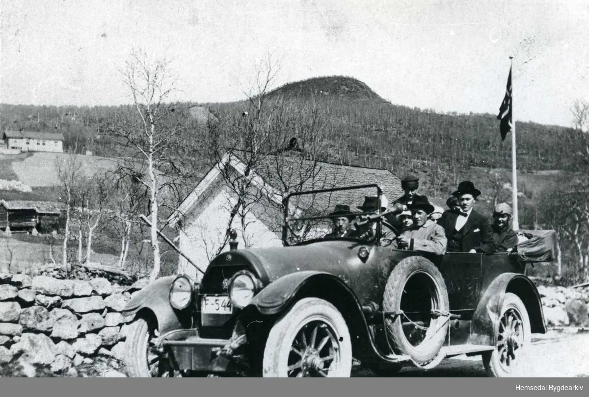 Biletet er teke ved skulehuset i Lio då Hans Lien og Ingebjørg Torset gifta seg. Eirik E. Huso ved rattet. Bilen er ein F 544 Cadillac 1916 mod. Til venstre i framsetet sit Knut E. Thorset (Stuen)
Bak sjåføren, Eirik E. Huso, sit Torleiv A. Thorset og Ragnhild Mjølid.
