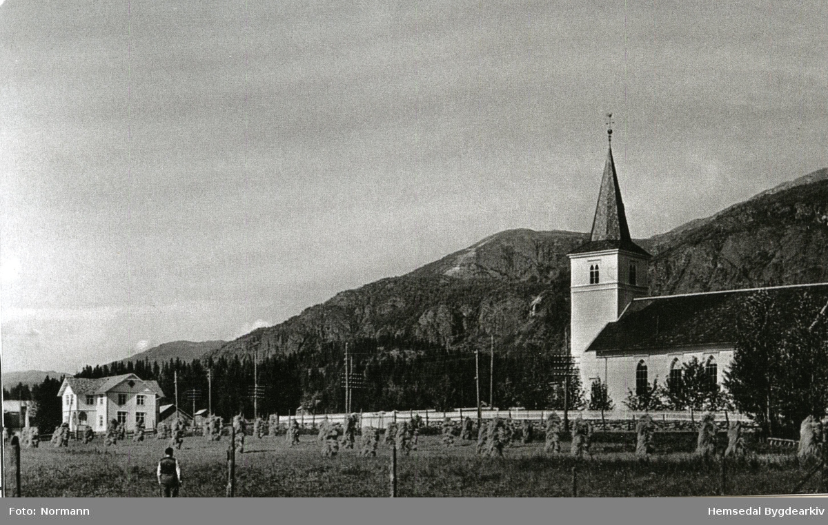 Hemsedal kyrkje med det gamle kommunehuset til venstre. Dette huset vart rive i byrjinga av 1980. I same området vart Kyrkjestugo sett opp i 1981.
I framgrunnen ser ein korn på staur som var vanleg den gongen.