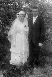 Portrett i helfigur av et brudepar. Bildet er tatt utendørs.