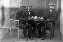 Studioportrett av tre menn rundt et bord.