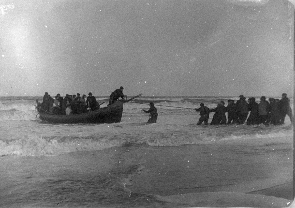 Livbåt full av folk dras i iland på strand.
