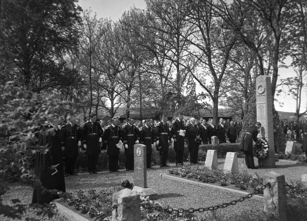 Engelsk gravsted. Bekransning av minnesmerke, med prest, uniformerte herrer, matroser og folkemengde.