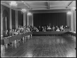 Gruppe menn med langbord (provisoriske) med talerstol. Diver