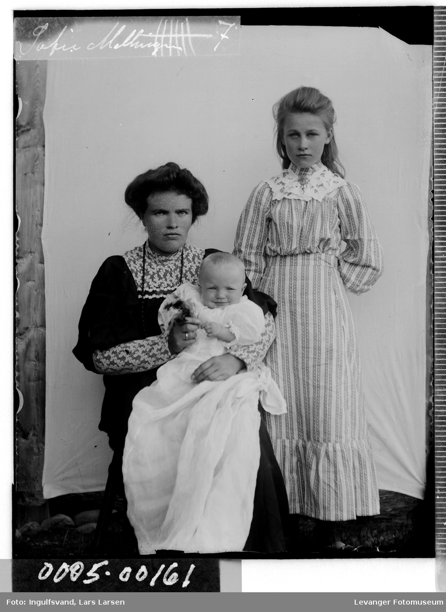 Gruppebilde av kvinne, jente og et spedbarn iført dåpskjole.
