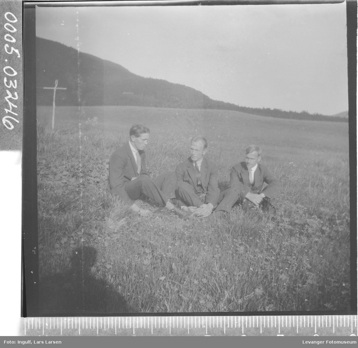 Gruppebilde av tre menn som sitter i en eng.