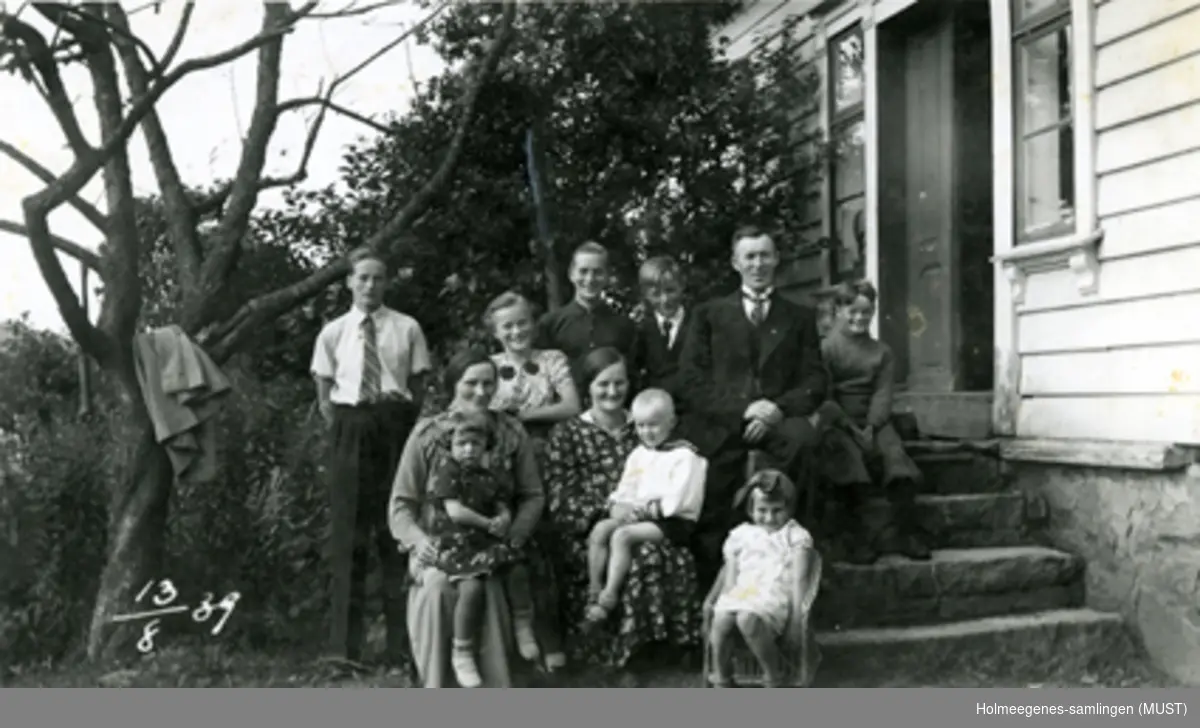 Gruppebilde tatt ved trappa til et bolighus, familiebilde med 11 personer.
