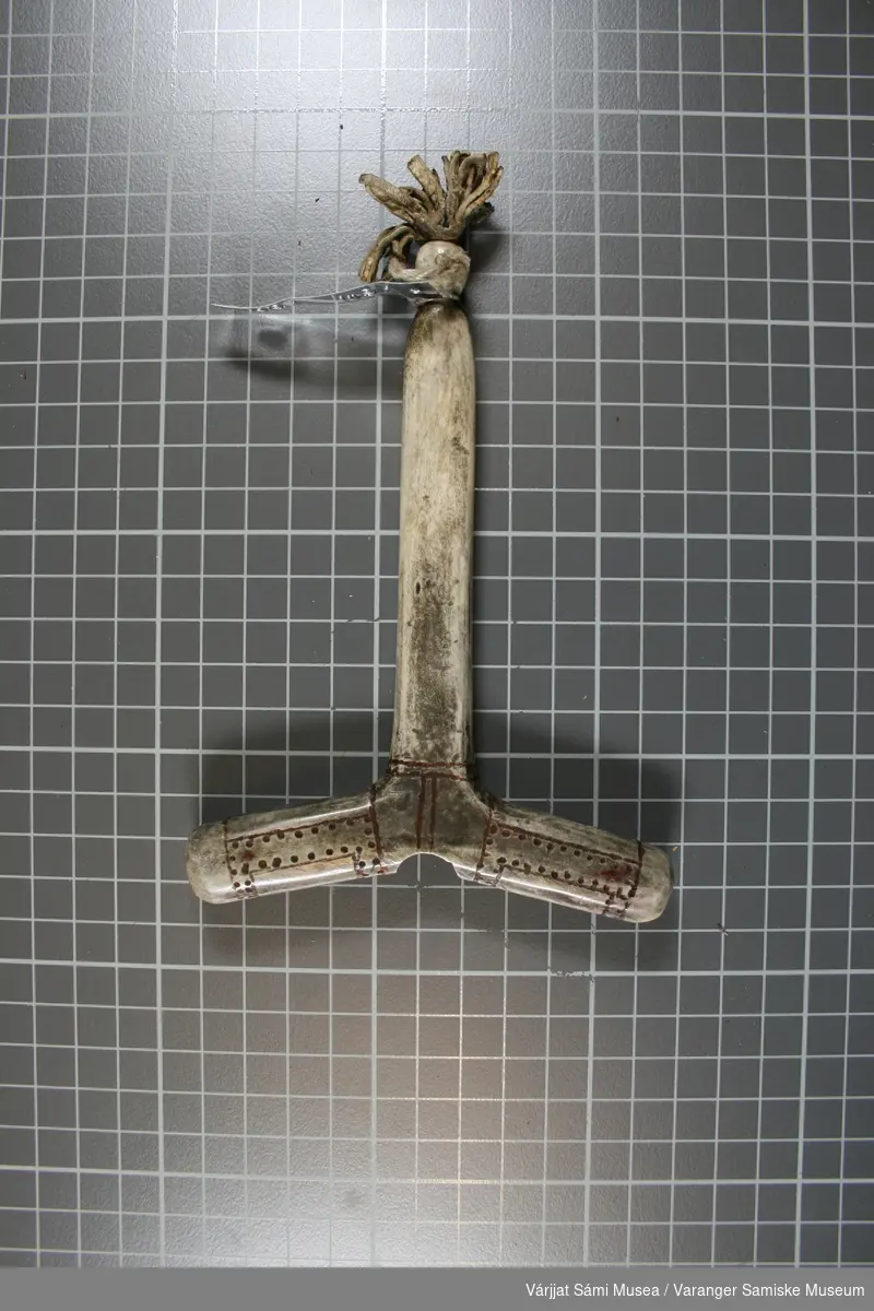 Moderne replika av hammer til runebomme / sjamantromme. Hammeren er laget av horn. Den er grå og har noen skinnbiter som henger nederst. .