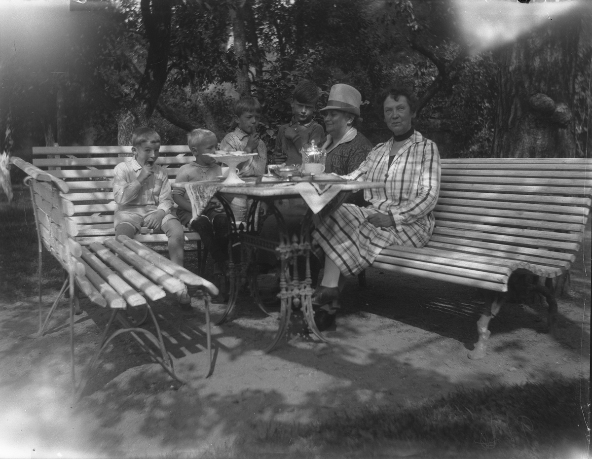 To kvinner og fire gutter rundt bord under trær