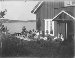 Gruppe kvinner og menn på veranda ved sjøen. Kragerø