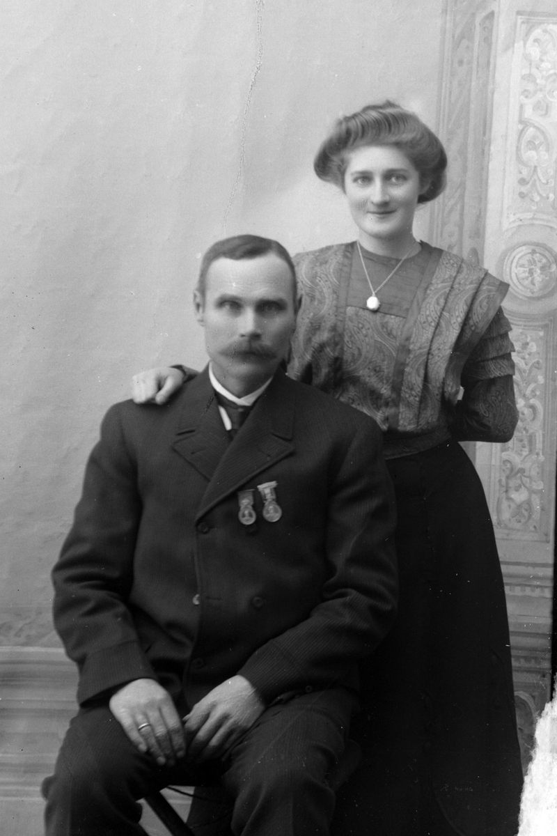 Studioportrett av en mann som sitter foran en stående kvinne.