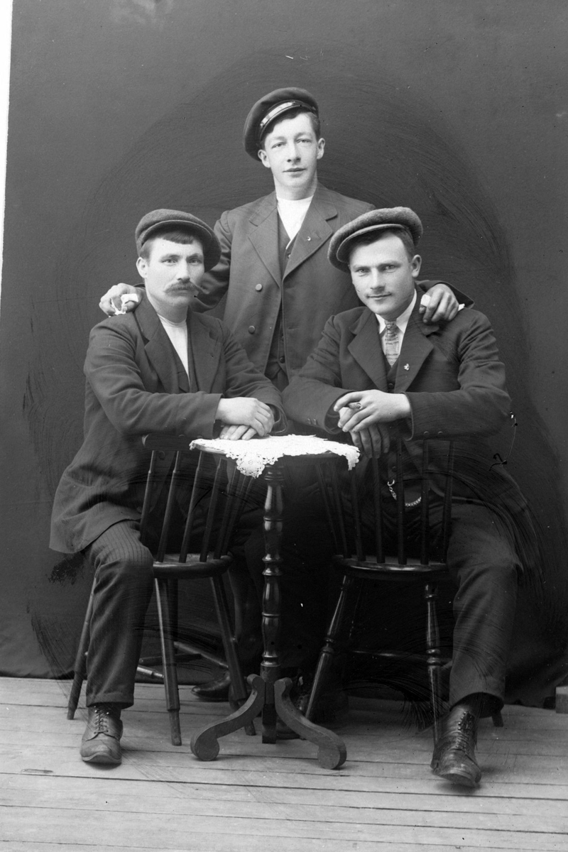 Studioportrett av tre menn rundt et bord.