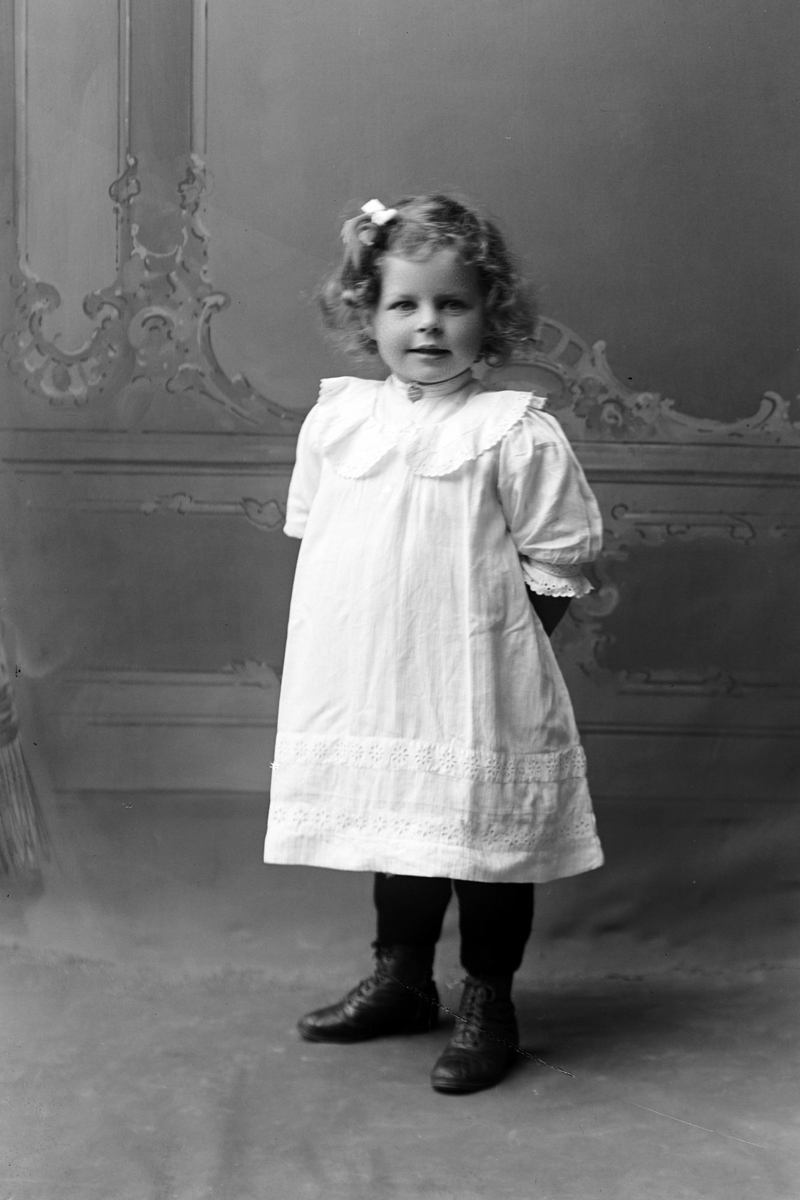 Studioportrett av en liten jente i en lys kjole.