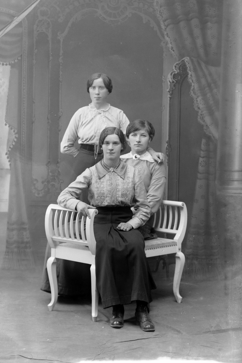 Studioportrett av to kvinner som sitter foran én som står.