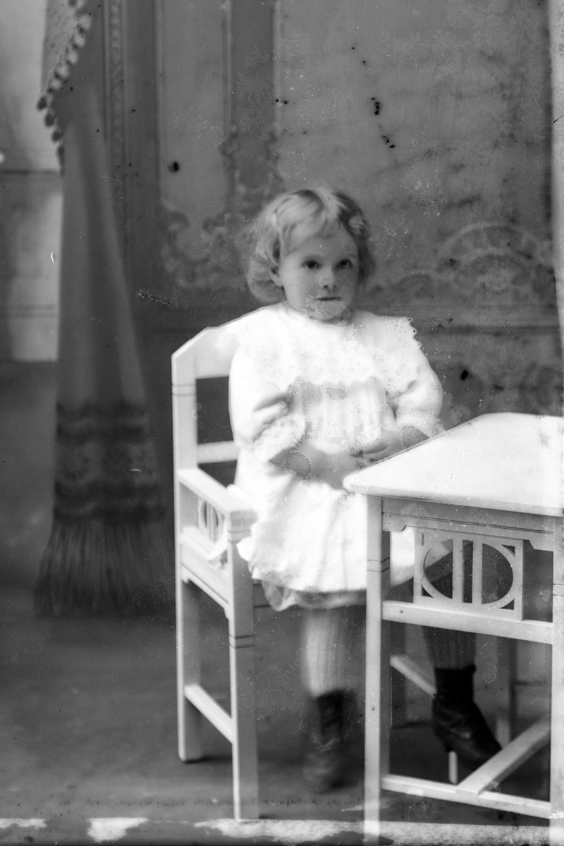 Studioportrett av liten jente i en stol.