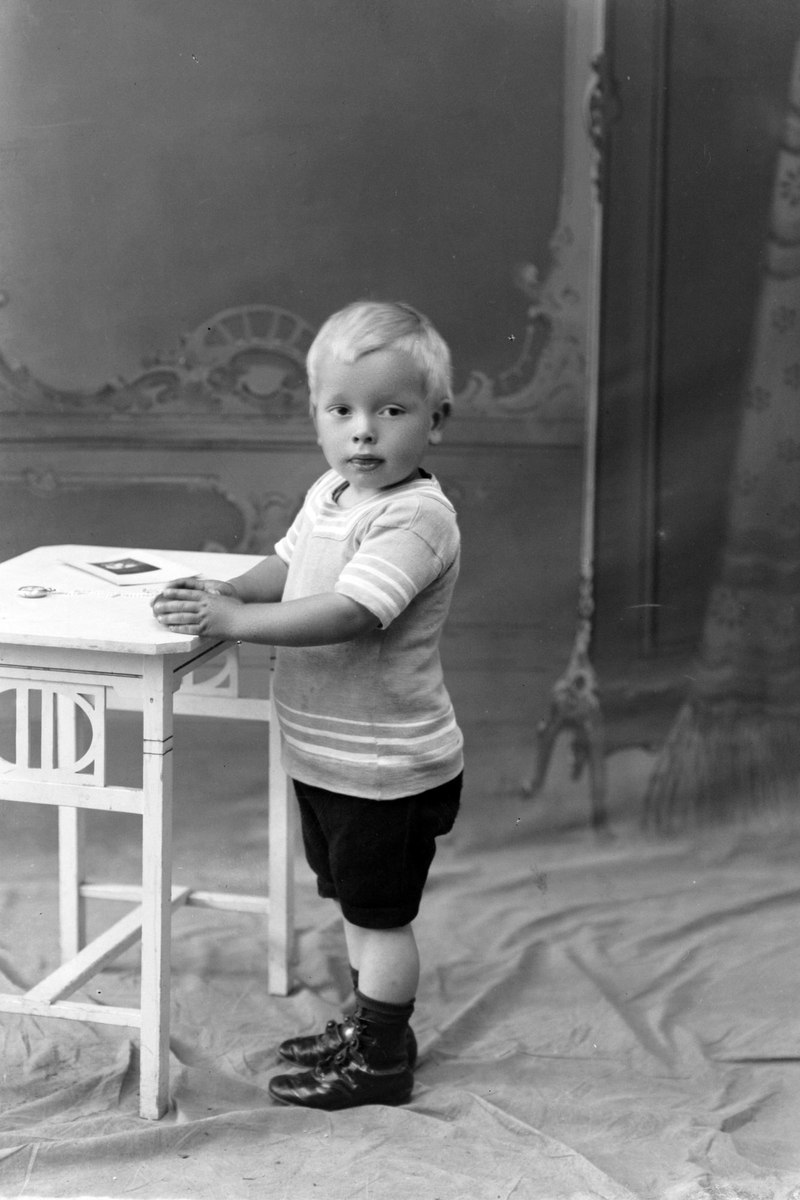 Studioportrett av en liten gutt ved et bord.