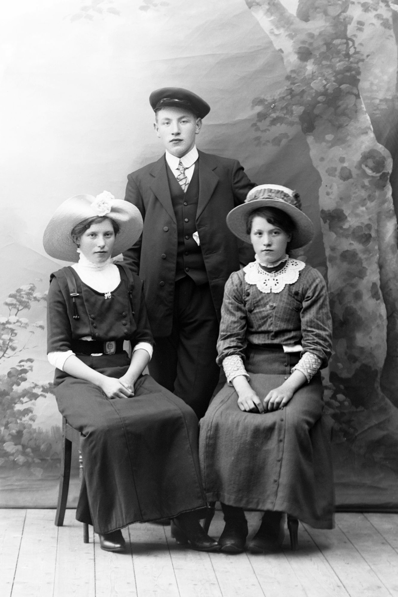 Studioportrett av en ung mann stående bak to jenter.