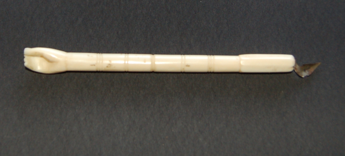 Penneskaftet er skoret ut av eit selbein og forma som ei hand med fingrar i eine enden, og med holder for pennesplitt i den andre.
