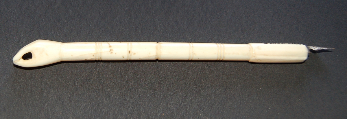 Penneskaftet er skoret ut av eit selbein og forma som ei hand med fingrar i eine enden, og med holder for pennesplitt i den andre.
