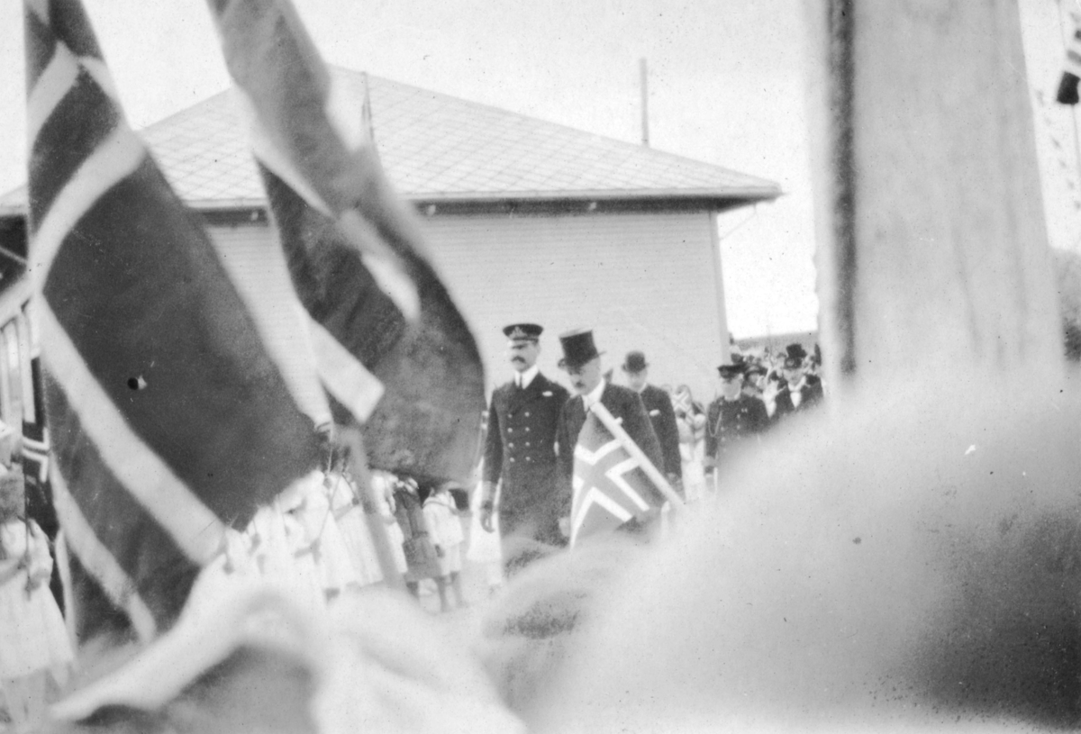Da kongen var på besøk i Finnmark i 1922. På bildet er han sammen med fylkesmann Hagbart Lund. Det er flere menn som kommer gående etter dem. Mange norske flagg er framme